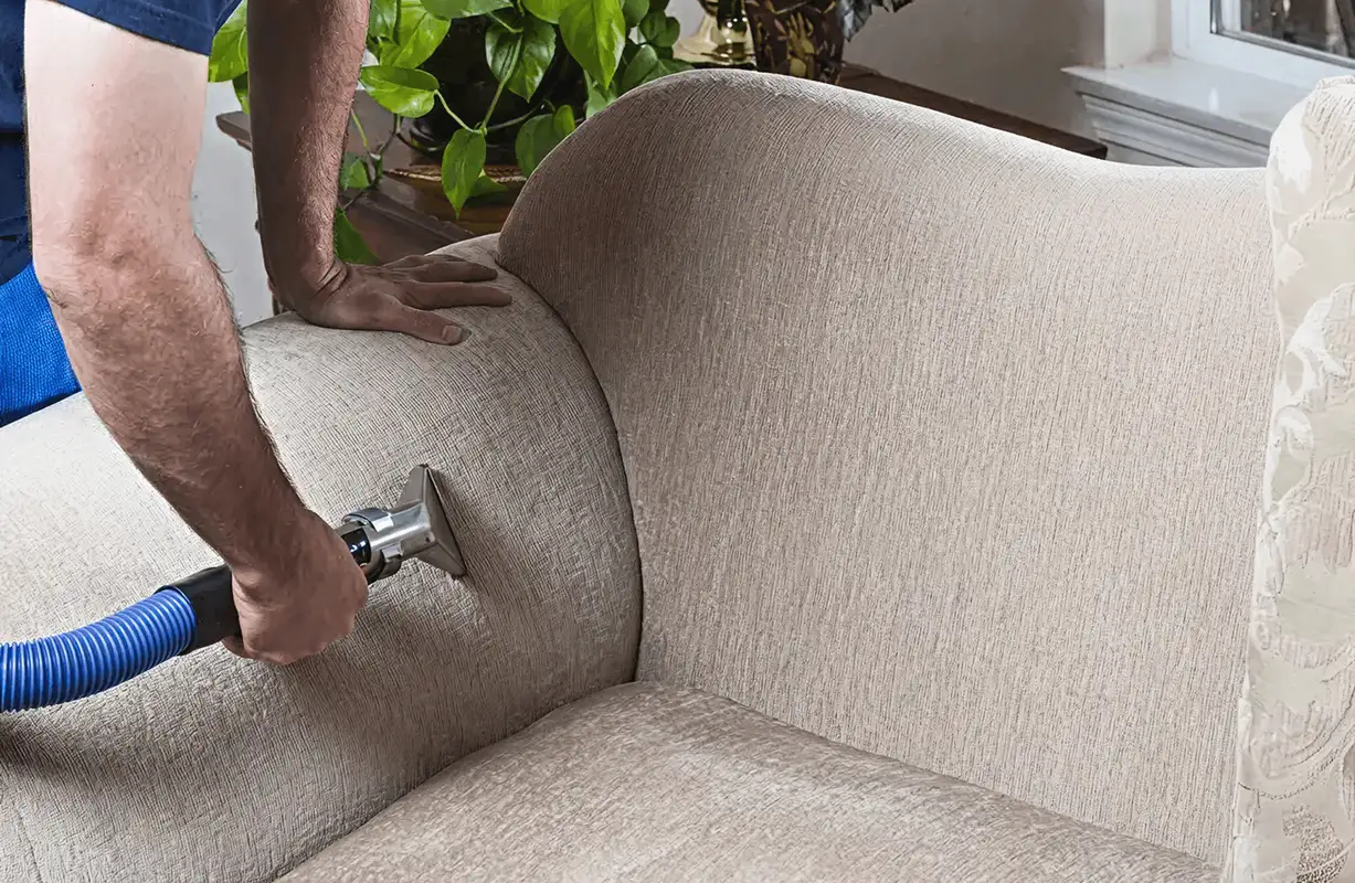 Professional upholstery cleaner deep-cleaning a fabric sofa with a handheld extraction tool and hose, Ogden, UT.